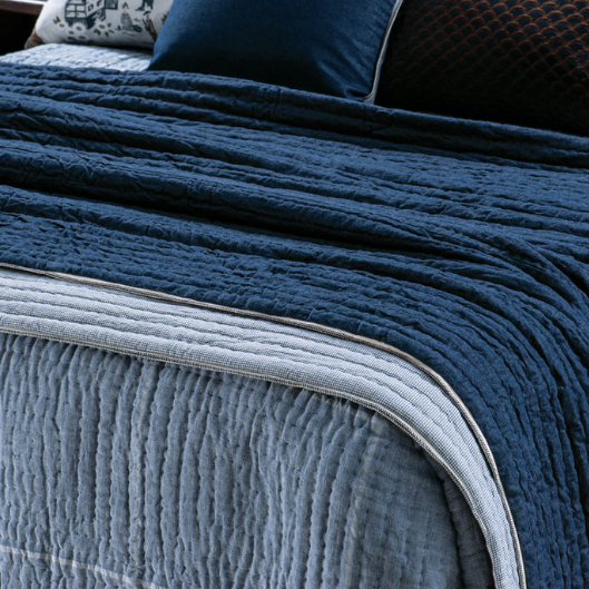Bring your bedroom to life with this luxuriously soft cotton and linen hand quilted throw.   This contemporary and reversible coverlet features a denim cotton front and a woven silver and indigo linen with small check design on the reverse.   This sophisticated piece includes lines of hand-quilting, filled with cotton wadding and finished with a contrasting woven ribbon in graphite and ivory.  Colour: denim  Composition: 100% cotton outer with cotton wadding   Dimensions: 240cm x 220cm 